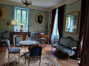 A room with a round table, chairs, a sofa, a mirror, and a window with curtains. - Large family home in the heart of nature near the Brière regional park (12p) (Saint-Lyphard)