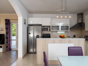 A modern kitchen with a central island, stainless steel appliances, and a dining area with a purple chair. - Four Bedroom Villa, Terrace, Pool (Pridvorje)