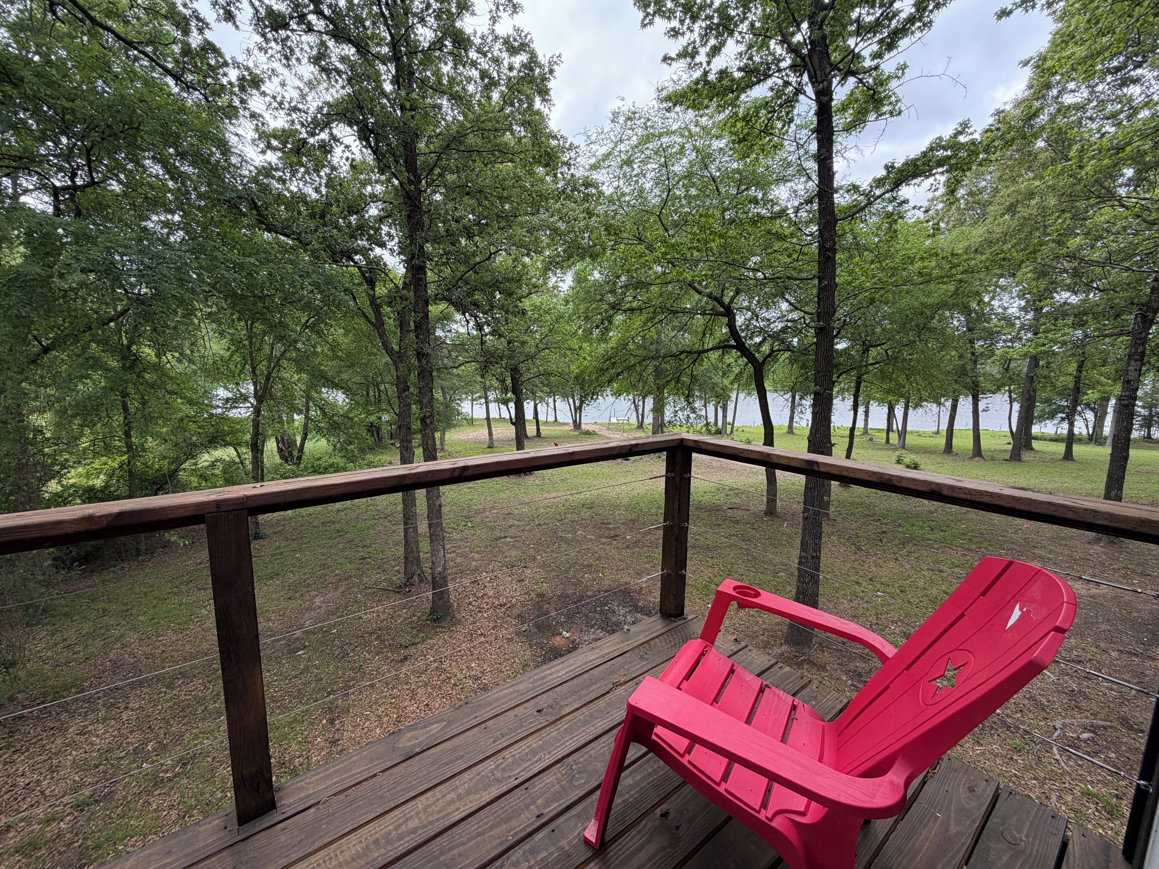 Une terrasse en bois avec un fauteuil Adirondack rouge, entourée d’arbres et offrant une vue sur un lac.