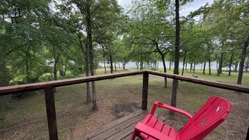 Une terrasse en bois avec un fauteuil Adirondack rouge, entourée d’arbres et offrant une vue sur un lac.