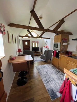 Une cuisine avec des poutres en bois, un coin repas avec une table et des chaises, et un salon avec un canapé et une télévision.