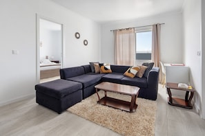 A modern living room with a sectional sofa, a coffee table, a rug, and a view of the balcony.
