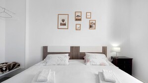 Een tweepersoonsbed met bloemenkussens, een houten hoofdbord, een nachtkastje met een lamp, en een muur met ingelijste foto's.