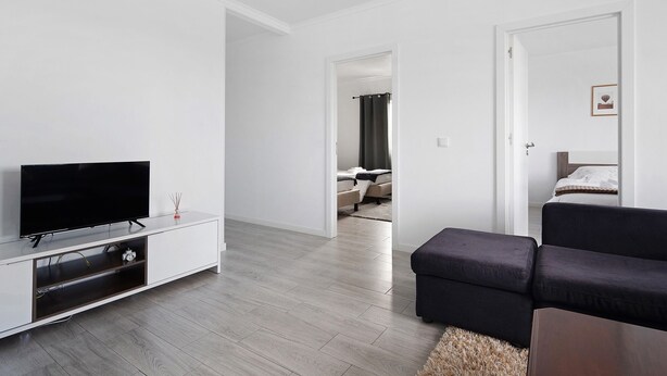Een moderne woonkamer met een flatscreen televisie, een donkere bank en een houten tv-meubel.