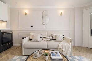 Ein modernes Wohnzimmer mit einer Couch, einem Couchtisch mit Büchern und einer Kerze sowie einer Wandleuchte.