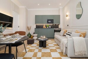A modern living room with a checkered floor, a sofa, a coffee table, and a dining area with a table set for two. - Nice apartment 1BDR/4PAX in Opera (Paris)