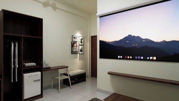 Una habitación moderna con televisión de pantalla plana, escritorio, silla, armario y un refrigerador pequeño.