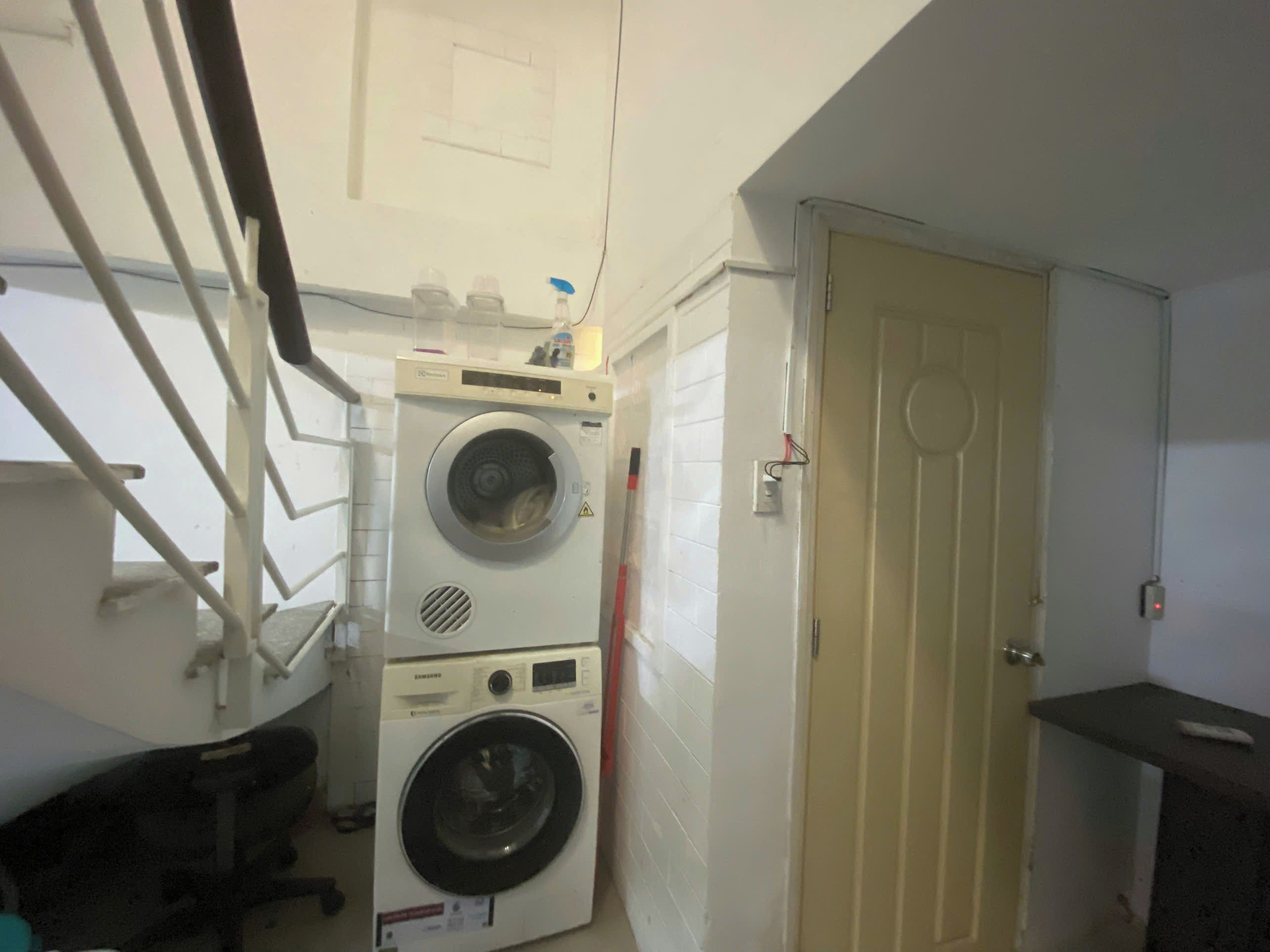 Une petite buanderie comprenant un lave-linge, un sèche-linge, une porte et une petite étagère.