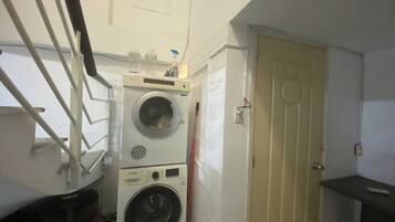 Une petite buanderie comprenant un lave-linge, un sèche-linge, une porte et une petite étagère.