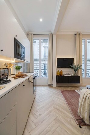 A modern kitchen with a built-in microwave, a toaster, and a bread loaf on the counter. There is a flat-screen TV mounted above a dark-colored console table. - Nice apartment 1BDR/4PAX in Opera (Paris)