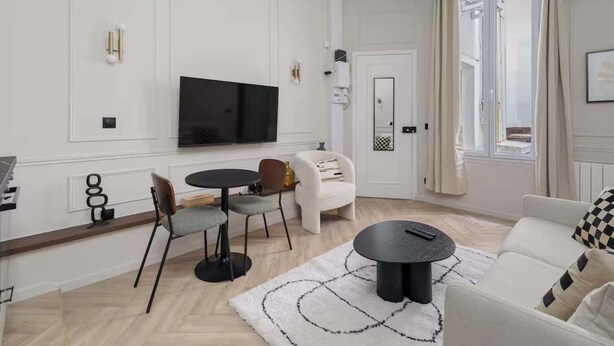 Una sala de estar moderna con una televisión de pantalla plana, una mesa redonda de comedor con sillas, un sofá y un tapete estampado.