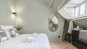 Un dormitorio ordenado con cama, mesita de noche, cómoda, espejo y ventana con cortinas.