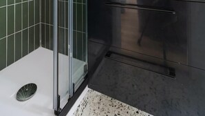 Un baño moderno con cabina de ducha de vidrio, un lavabo negro y un espejo redondo.