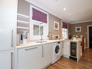 A modern kitchen with a built-in washing machine, a water dispenser, and a window with a purple valance. - Tickety-boo (Broadstairs)