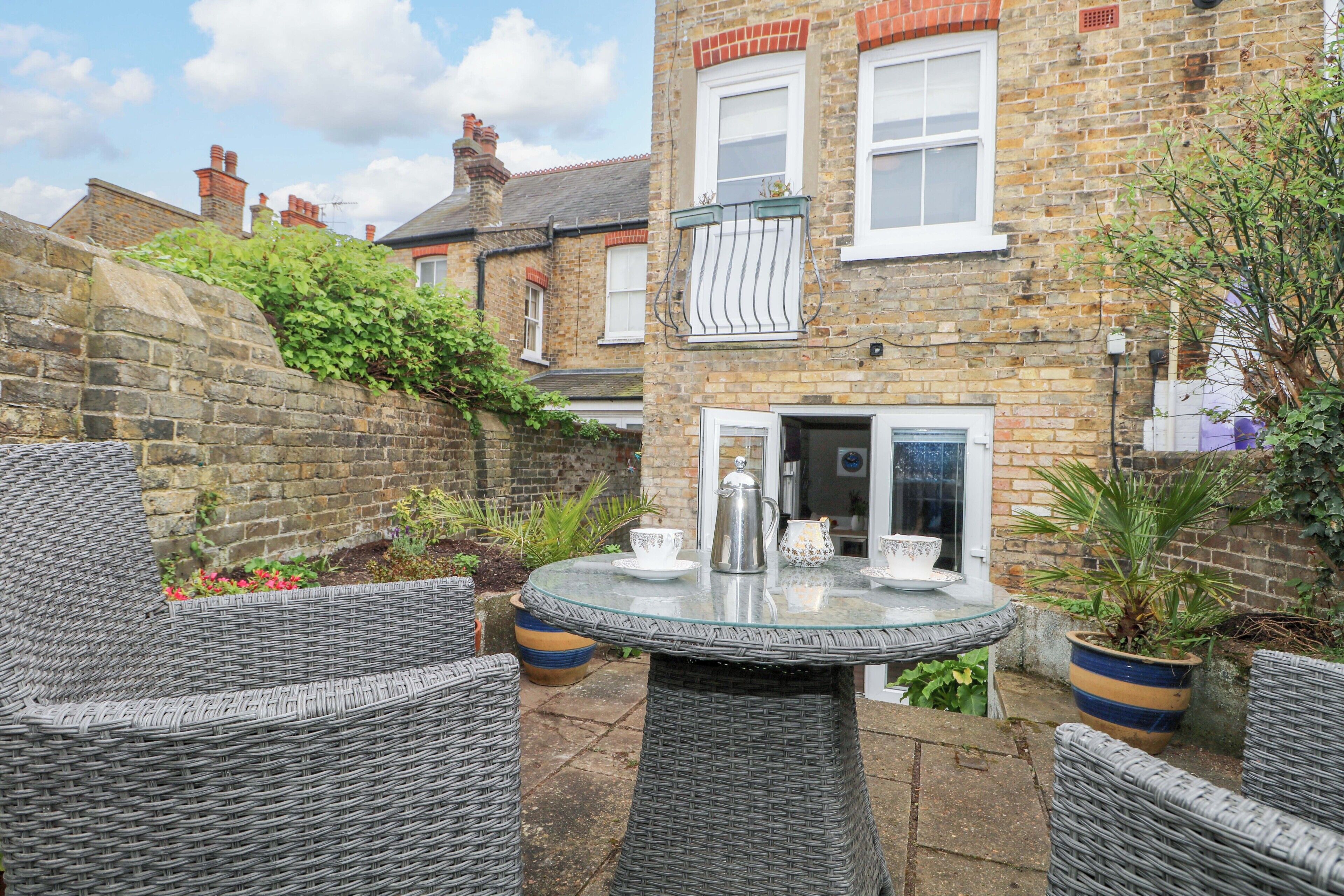 A courtyard with wicker furniture, a glass table, and a brick house with a door and windows.