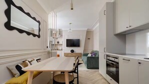 Une cuisine moderne avec un coin repas, un téléviseur fixé au mur et un four encastré.