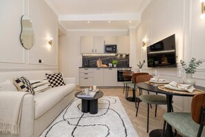 Ein modernes Wohnzimmer mit Sofa, Couchtisch und Essbereich mit Stühlen sowie einem Fernseher.