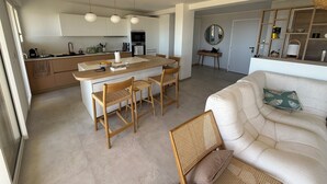 A modern kitchen with a central island, dining area with chairs, a sofa, and a mirror. - VAL D'AZUR Panoramic Sea View - Air-conditioned 4-room apartment - Center and Beach (Bandol)