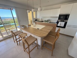 A modern kitchen with a central island, wooden chairs, and a view through large windows. - VAL D'AZUR Panoramic Sea View - Air-conditioned 4-room apartment - Center and Beach (Bandol)