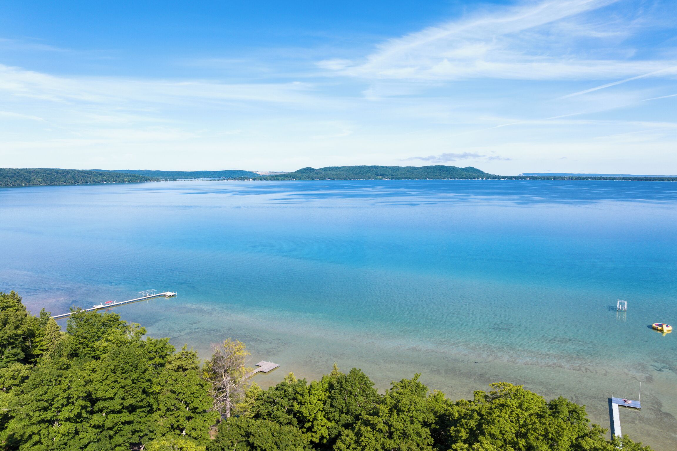A coastal view with a pier extending into calm waters, surrounded by dense green forest.