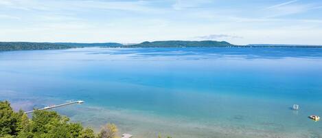 A coastal view with a pier extending into calm waters, surrounded by dense green forest.