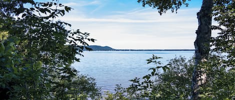 Un paysage naturel comprenant une étendue d’eau, des arbres et une chaîne de montagnes à l’horizon.