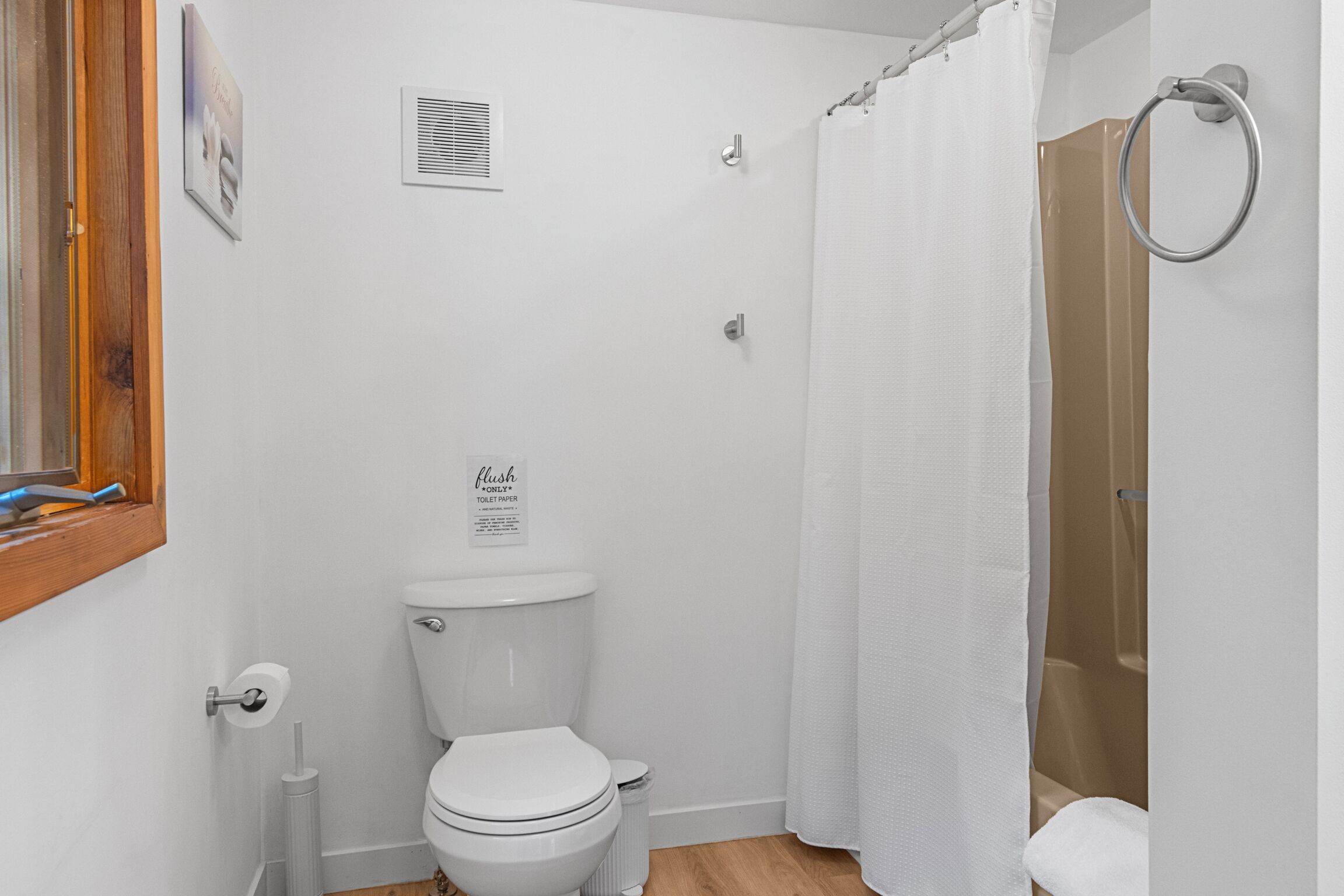 A bathroom with a toilet, a shower curtain, a toilet paper holder, and a sign on the wall.