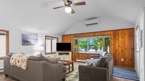 A living room with a ceiling fan, a flat-screen TV, and wooden paneled walls. - Have Lazy Days at Lazy Bear Landing on Glen Lake (Maple City)