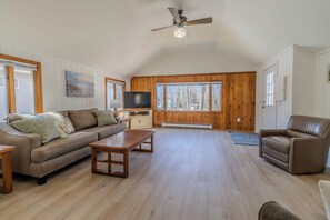 A spacious living room with a wooden ceiling, a sofa, a coffee table, a TV, and a fireplace.