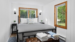 A bedroom with a bed, two bedside tables, a bench, and two windows with blinds. - Have Lazy Days at Lazy Bear Landing on Glen Lake (Maple City)