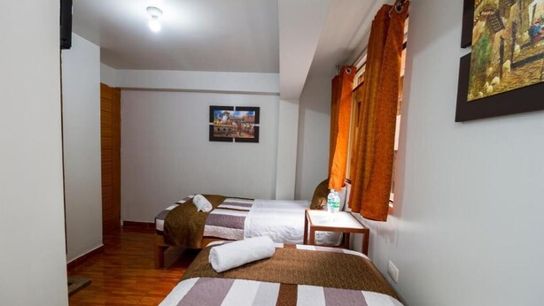 A room with two beds, a wooden floor, a small table with a bottle, and a painting on the wall. - Machu Picchu Land (Aguas Calientes)