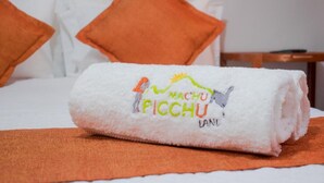 A neatly folded white towel with a logo and text on a bed with orange pillows. - Machu Picchu Land (Aguas Calientes)