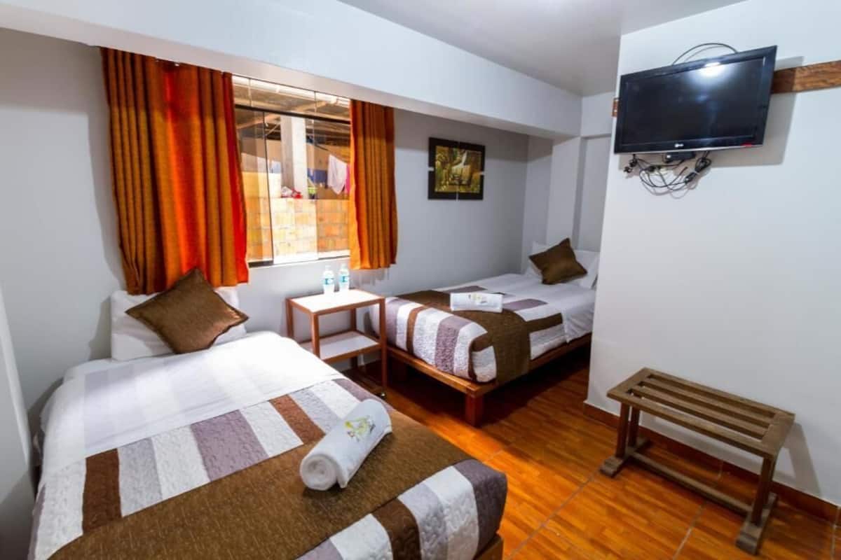 A hotel room with two beds, a TV, a small table, and a bench.