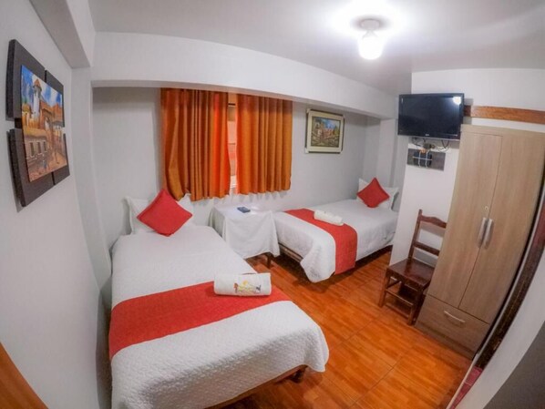 A hotel room with two beds, a TV, a wardrobe, and a small table.