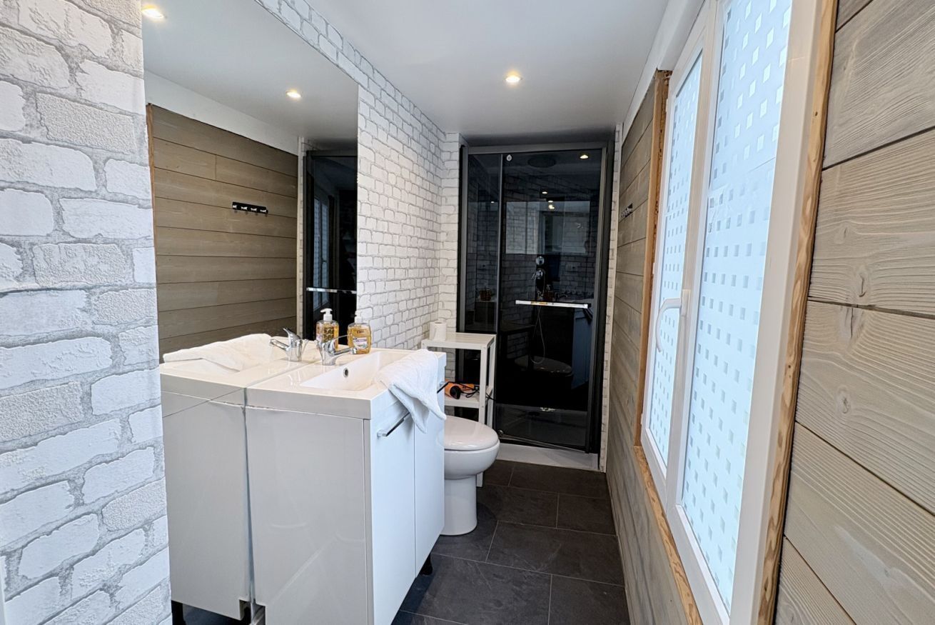 A modern bathroom with a white sink, mirror, and toilet, a glass shower enclosure, and a wooden wall.