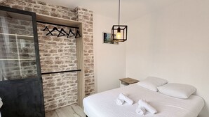 A bedroom with a bed, a wardrobe, a hanging light fixture, and a stone wall.