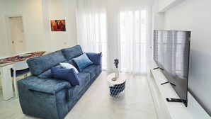 Ein modernes Wohnzimmer mit Sofa, rundem Couchtisch, Flachbildfernseher und Essbereich mit Tisch und Stühlen.