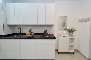 Una cocina moderna con armarios blancos, encimera negra, frutero, cafetera y un espejo decorativo.