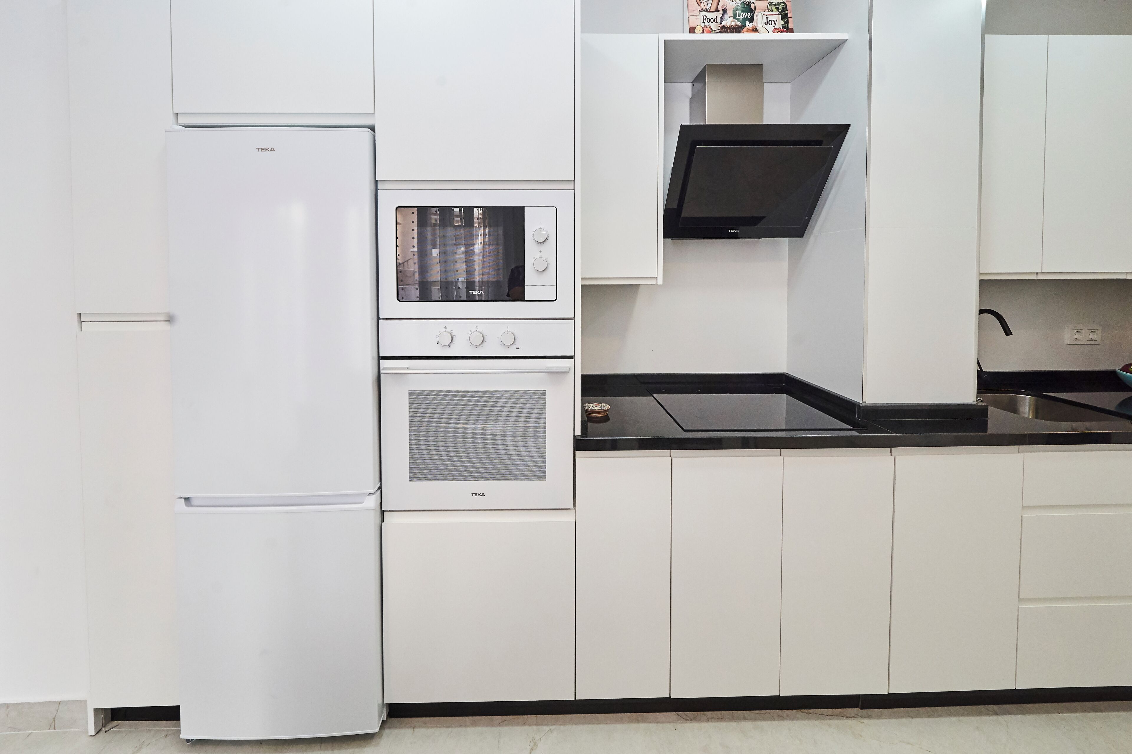 A kitchen with white cabinets, a built-in oven, a microwave, and a black countertop.