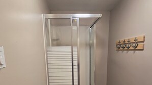 A glass-enclosed shower with a white door, a towel rack with wooden handles, and a small step leading to the shower area.