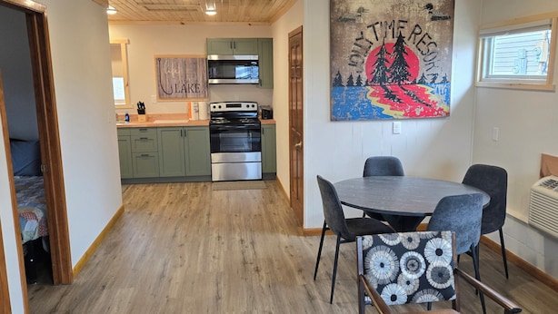 A modern kitchen with green cabinets, a microwave, and a stove. There is a dining area with a table and chairs.