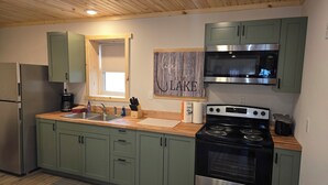 A modern kitchen with green cabinets, stainless steel appliances, a window, and a wooden ceiling.
