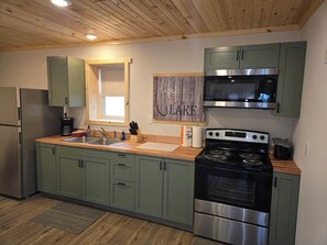 A modern kitchen with green cabinets, stainless steel appliances, a window, and a wooden ceiling.