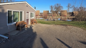 A cabin with a gravel driveway, wooden benches, and a pond.