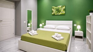Camera da letto moderna con parete verde accentata, un letto con biancheria bianca, un comodino con lampada e uno specchio.