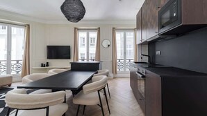 Una cocina moderna con encimera negra, microondas integrado y comedor con mesa negra y sillas blancas.