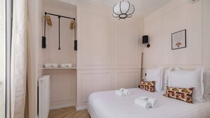 Habitación de hotel con cama, radiador, toallero e lámpara fijada a la pared.