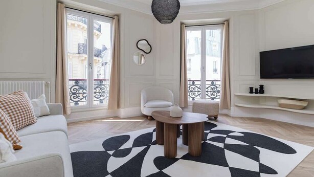 Una sala de estar moderna con un sofá, una mesa de centro, un televisor y un ventanal con vistas a edificios.