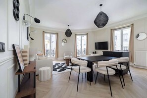 A modern living room with a dining area, large windows, and a flat-screen TV. - Spacious 6PAX flat in the city center (Paris)