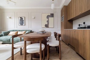 Un salon moderne avec une table à manger en bois, des chaises, un canapé vert et des œuvres d’art accrochées aux murs.